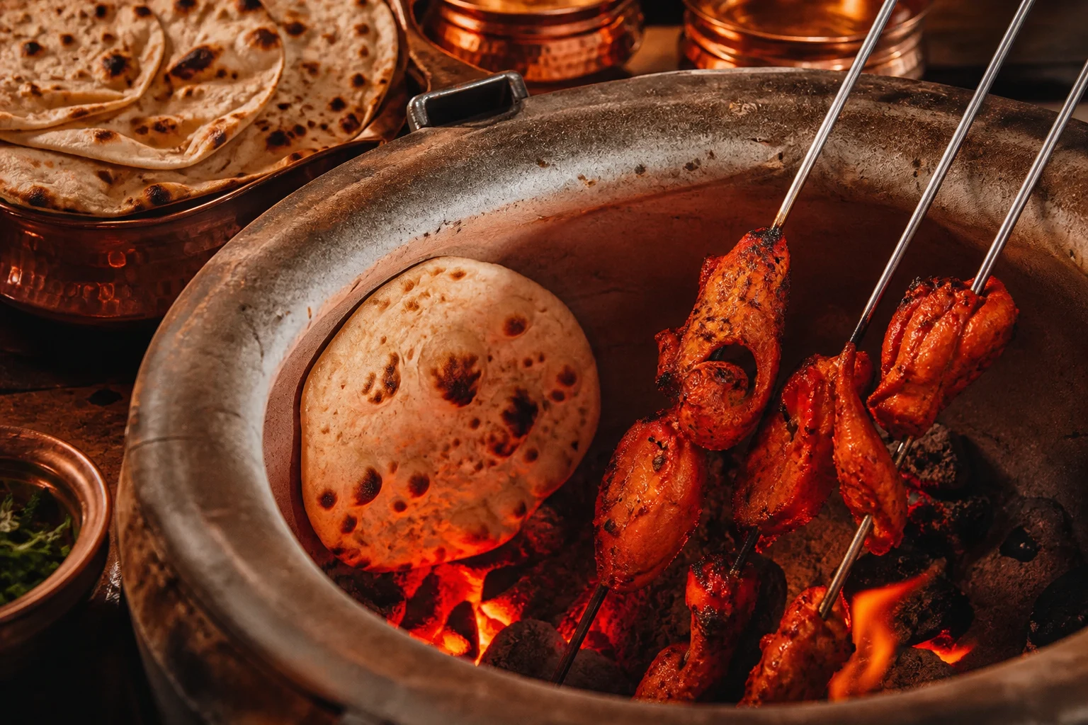 Naan and tandoori dishes cooking over glowing coals